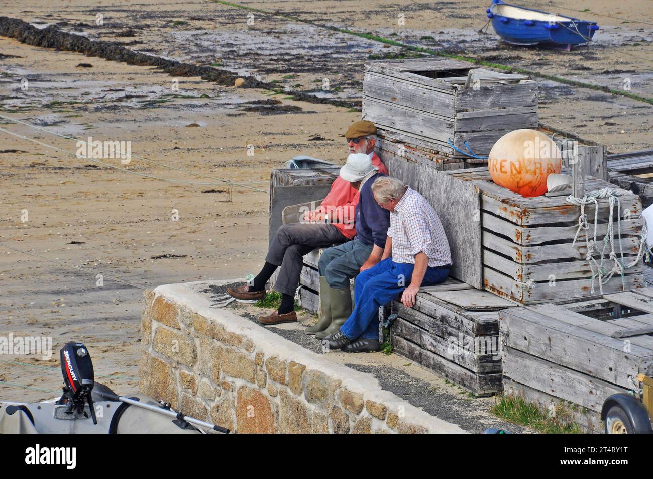 Three old gentlemen while away a bright autumn day putting the world to rights sat on crates overlooking the harbour beach in Hugh Town on St Marys, I Stock Photo