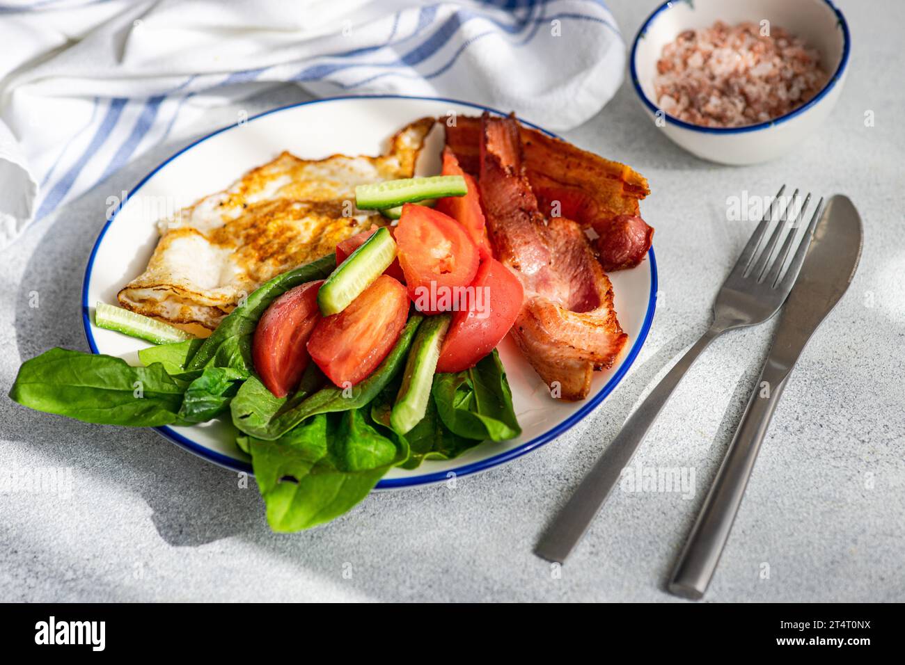 Close-up of a fried egg with bacon, spinach, tomato, cucumber and pink Himalayan salt Stock Photo