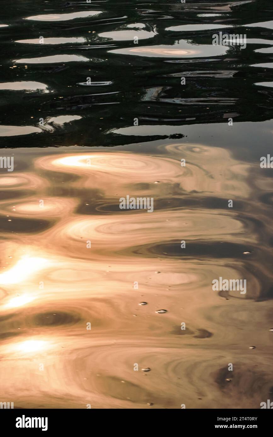 Water ripples and waves reflect the summer sun made hazy and dark by wildfire smoke on the ocean in Vancouver, Canada. Orange patterns and shapes. Stock Photo