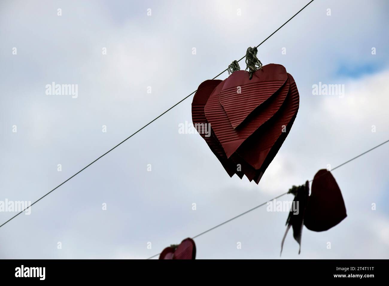 Street decoration. Several handmade red metal hearts hang on wire against cloudy sky. Valentine's Day Concept. Copy space. Selective focus. Stock Photo
