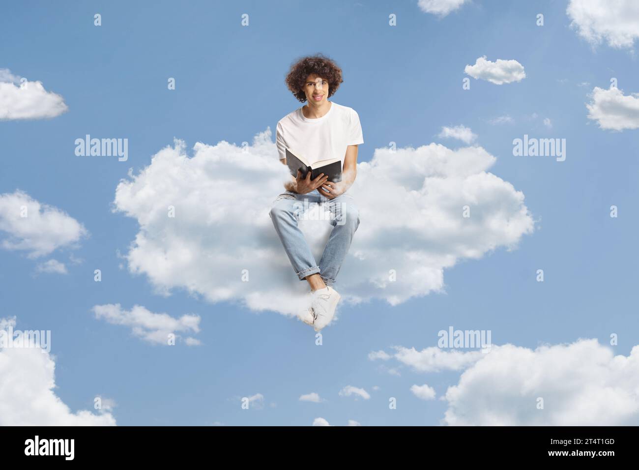 Young man with curly hair sitting on a cloud and holding an open book Stock Photo