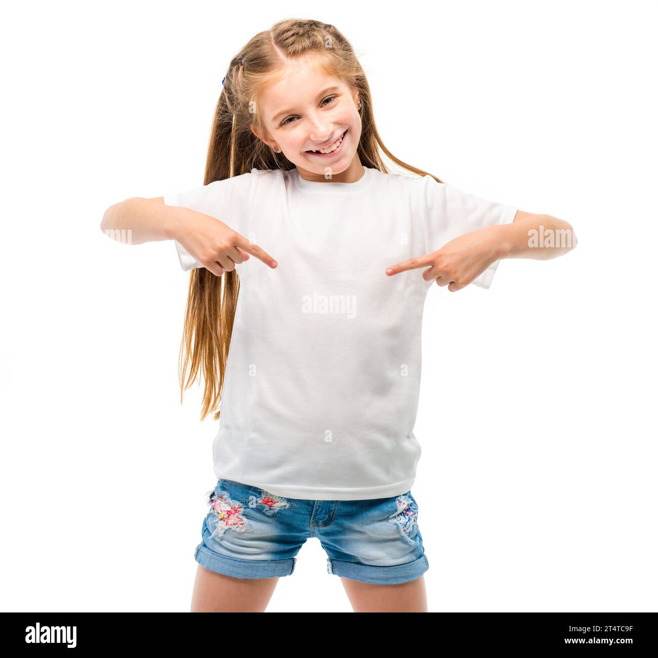 Positive little girl in casual white T-shirt indicates at blank space ...
