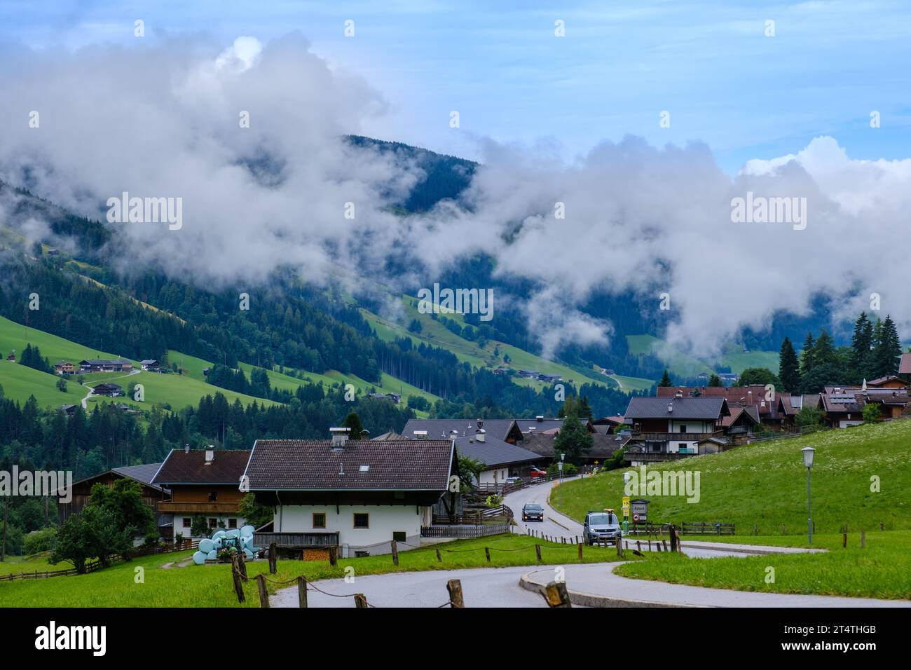 Village of Alpbach in Austrian Alps with traditional wooden houses, steep hills with meadows, tall trees & thick low clouds. Stock Photo