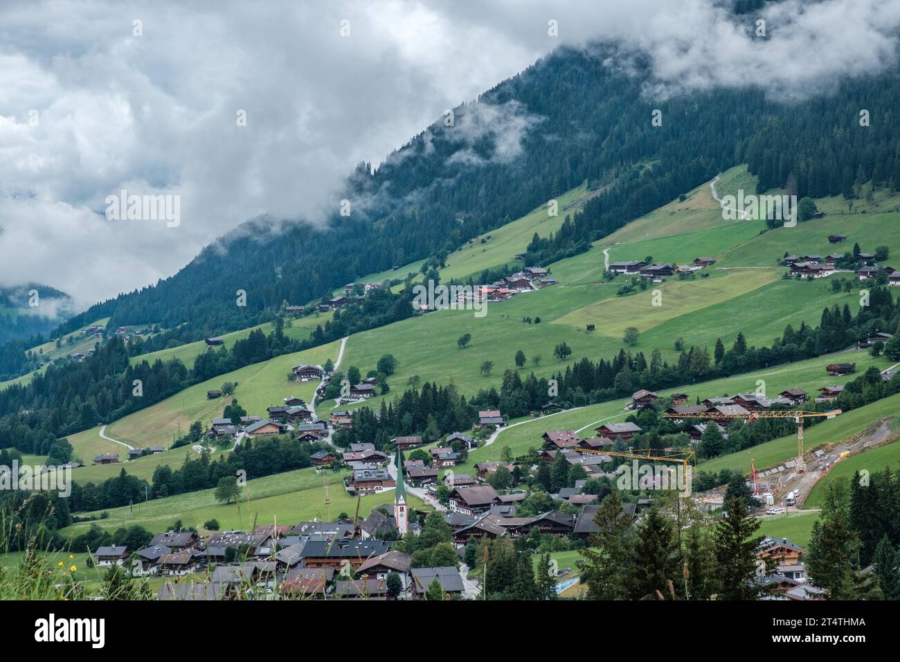 Picturesque village of Alpbach nestled among lush, rolling meadows, with misty low-hanging clouds & towering trees. Stock Photo