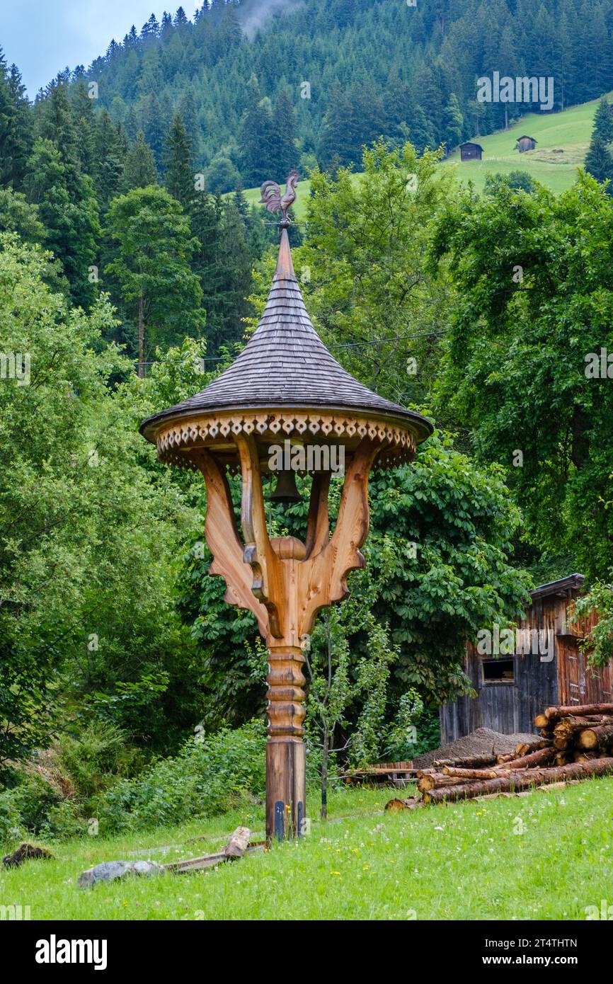Elaborately carved wooden post with bell, pointed roof & weather vane on top outside a home in the alpine village of Alpbach, Western Austria. Stock Photo