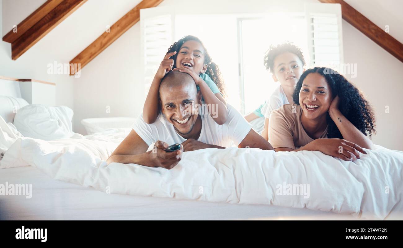 Funny, family portrait and watching tv in bedroom, bonding and sunshine with lens flare. Face, television and children with father, mother and happy Stock Photo