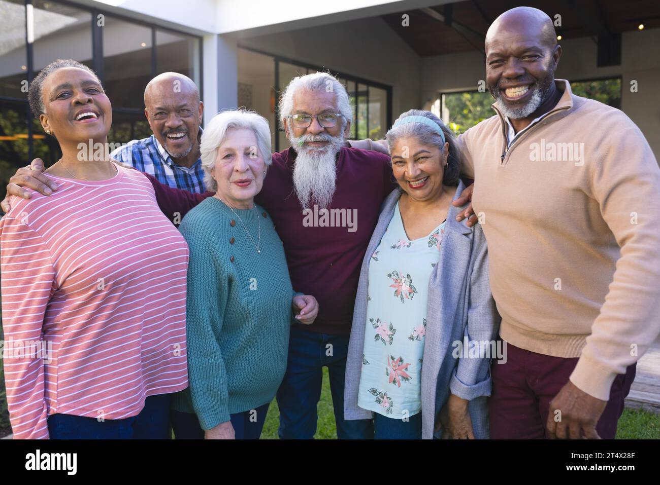 Happy diverse group of senior friends embracing next to house in sunny ...