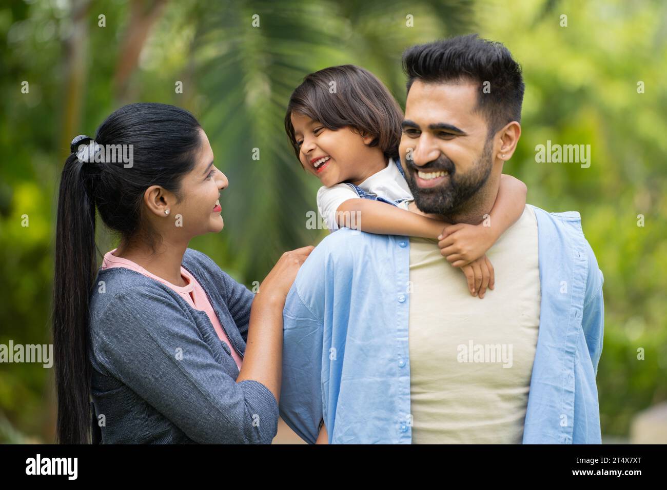 Happy indian father with girl kid as piggyback playing with mother at park - concept of family bonding, parenthood and weekend holidays Stock Photo