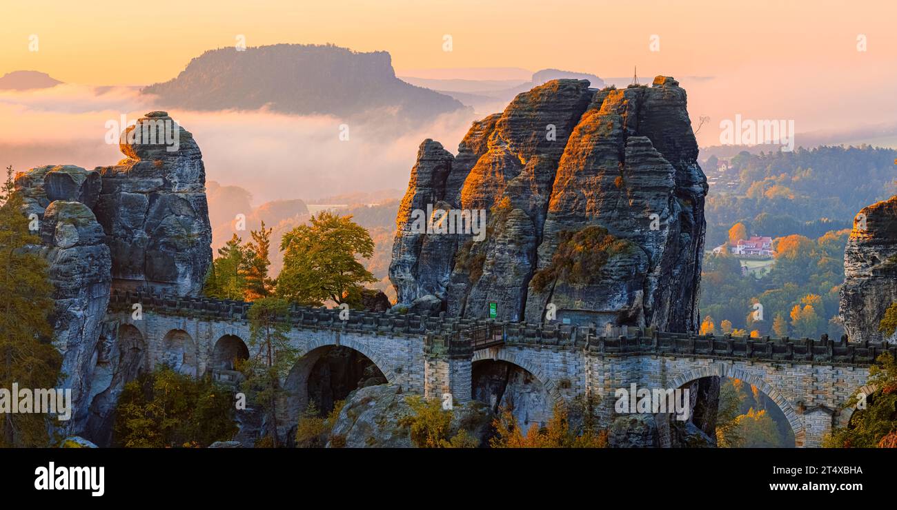 A wide 2:1 panoramic photo of an autumn sunrise with view from the Ferdinandstein with plenty of autumn colors at the Bastei Bridge, part of the Baste Stock Photo