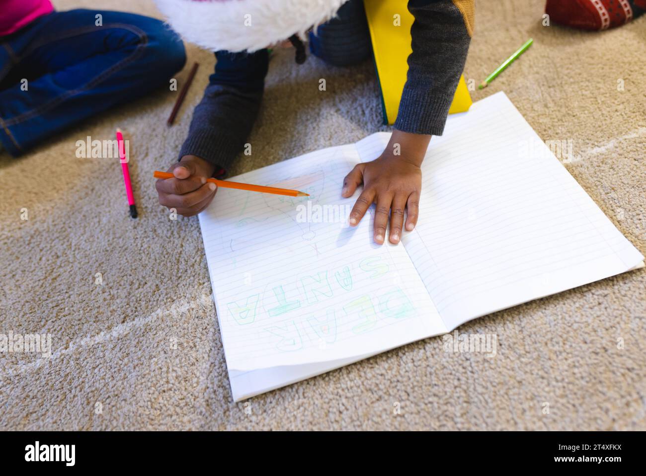 African american boy wearing christmas hat and drawing in notebook at home, copy space Stock Photo