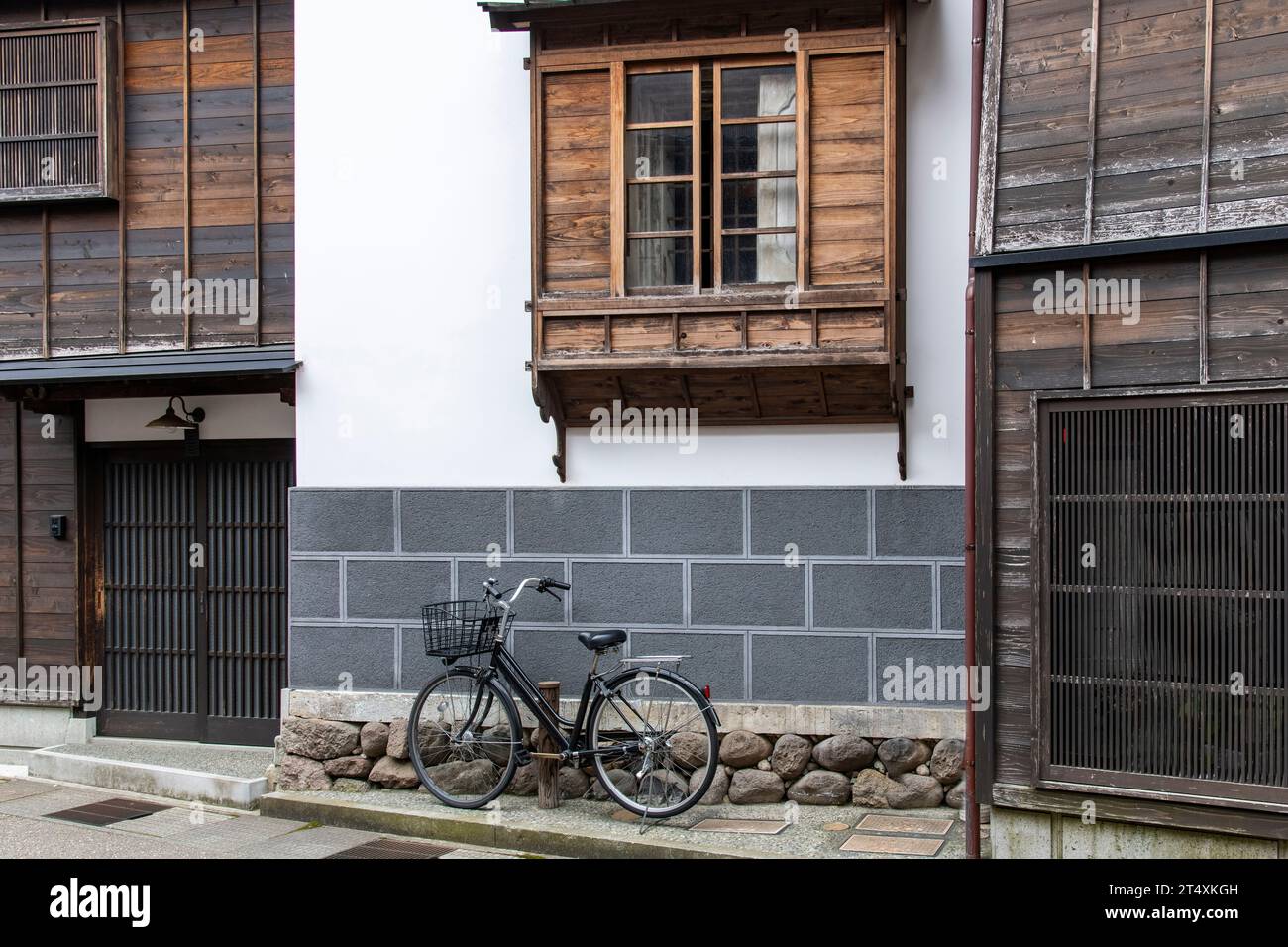 Urban street view of façade of typical Japanese house with modern stone and traditional wooden window and door features and bicycle parked in front of Stock Photo