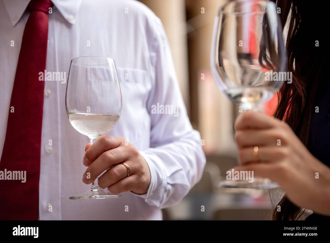 White vine glasses held in hand by a man and a woman, both wearing a wedding ring on their ring finger Stock Photo