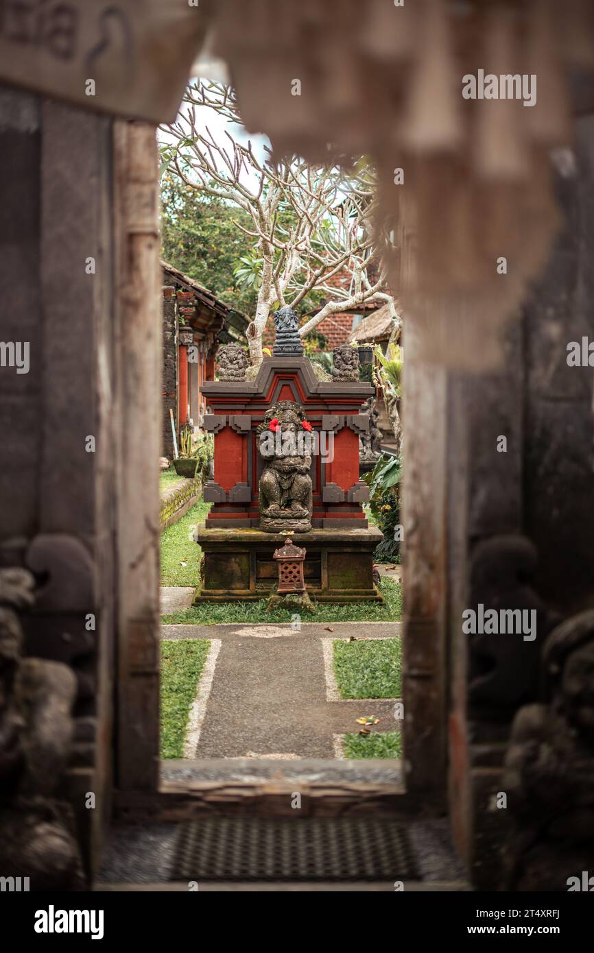 A stone archway leading to a small traditional Indonesian temple, adorned with intricate sculptures of historical figures Stock Photo