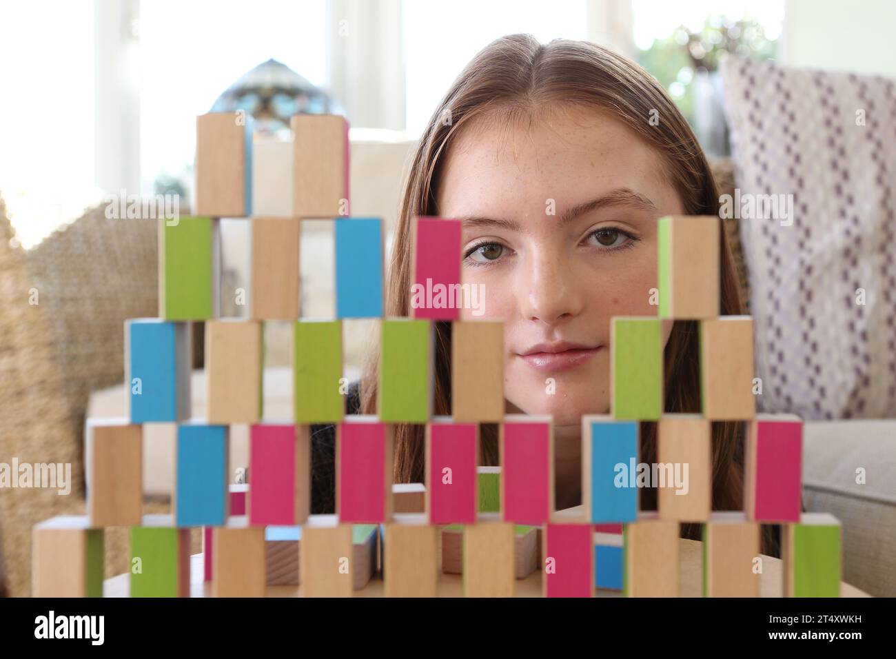 Teenage girl looking through a wall of wooden blocks with gaps, thoughtful and contemplating what she has built Stock Photo