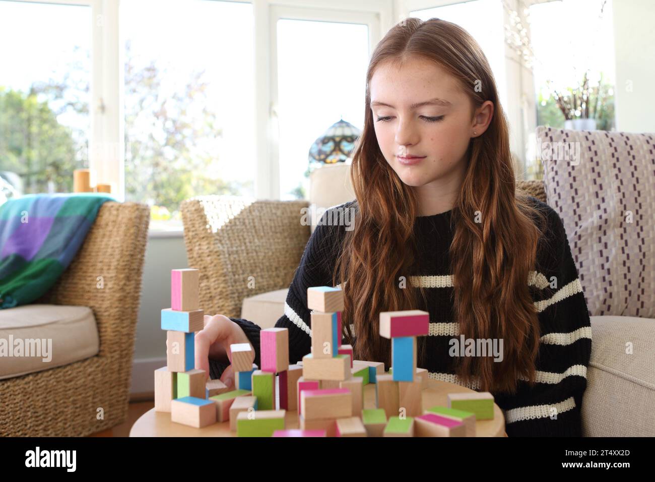 Teenage girl concentrating on building a wall of wooden blocks and towers Stock Photo