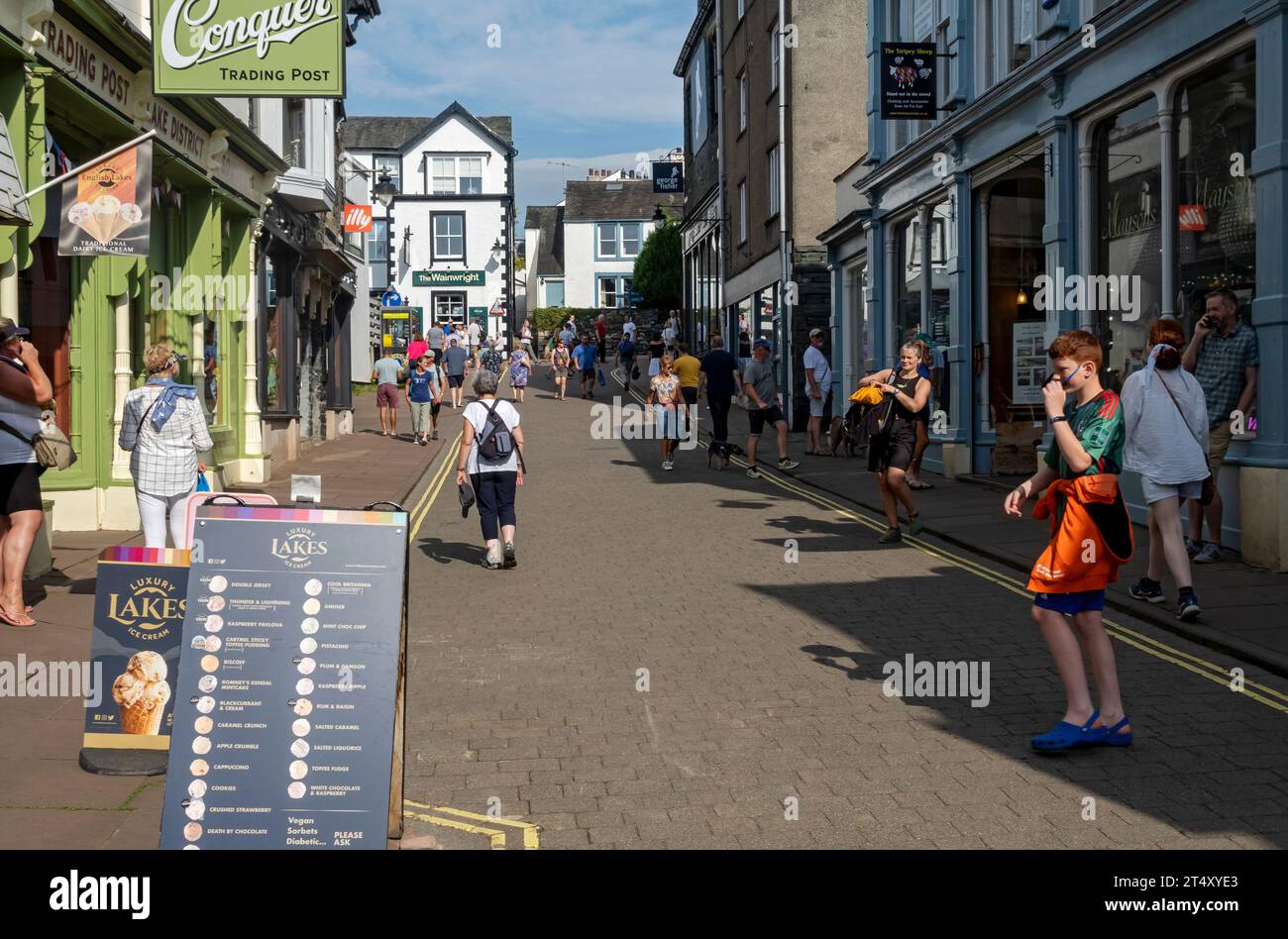 People tourists visitors walking by shops stores in the town centre street in summer Lake Road Keswick Cumbria England UK United Kingdom Britain Stock Photo