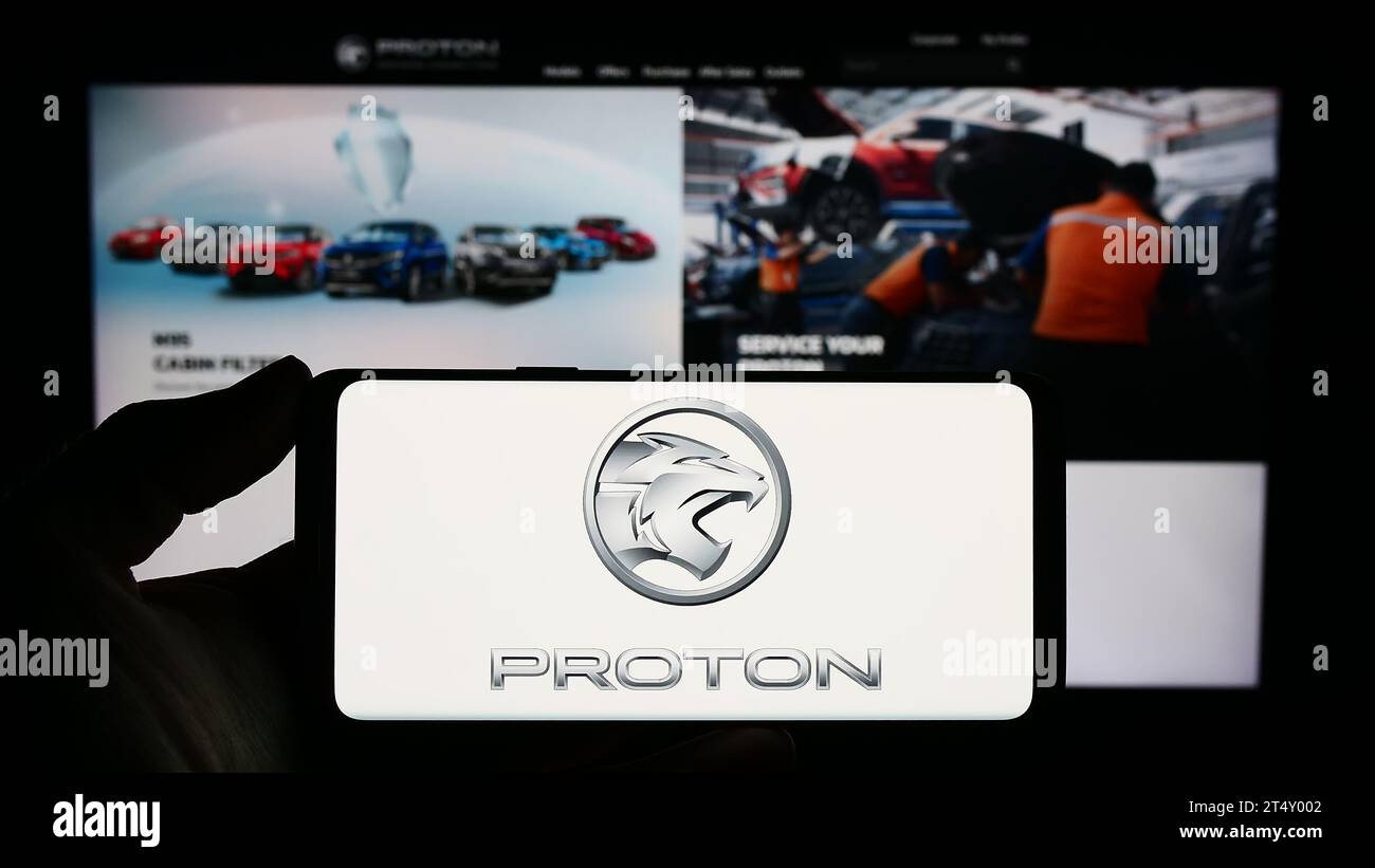 Person holding smartphone with logo of Malaysian automotive company Proton Holdings Berhad (PHB) in front of website. Focus on phone display. Stock Photo
