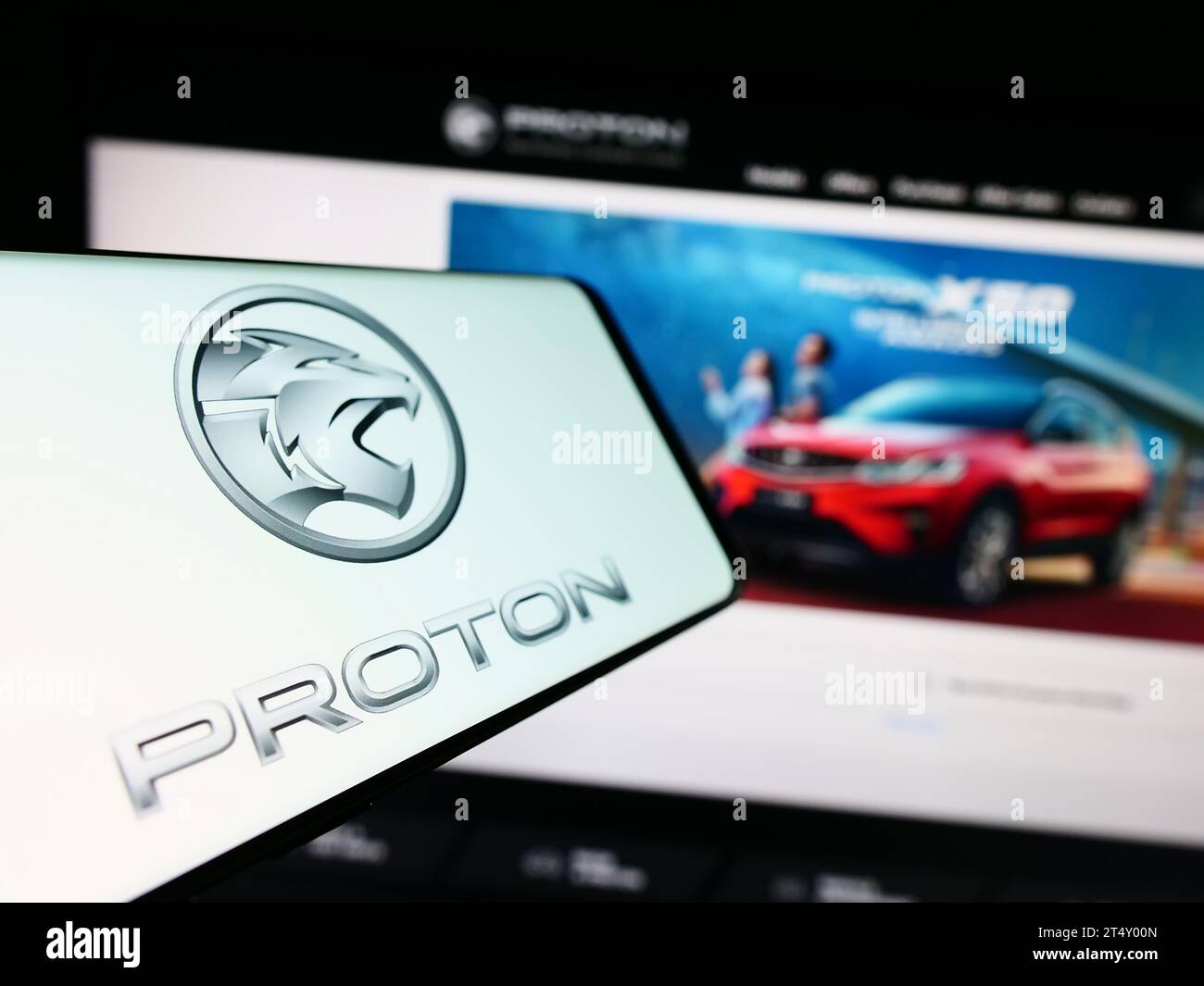 Smartphone with logo of Malaysian automotive company Proton Holdings Berhad (PHB) in front of website. Focus on center-left of phone display. Stock Photo