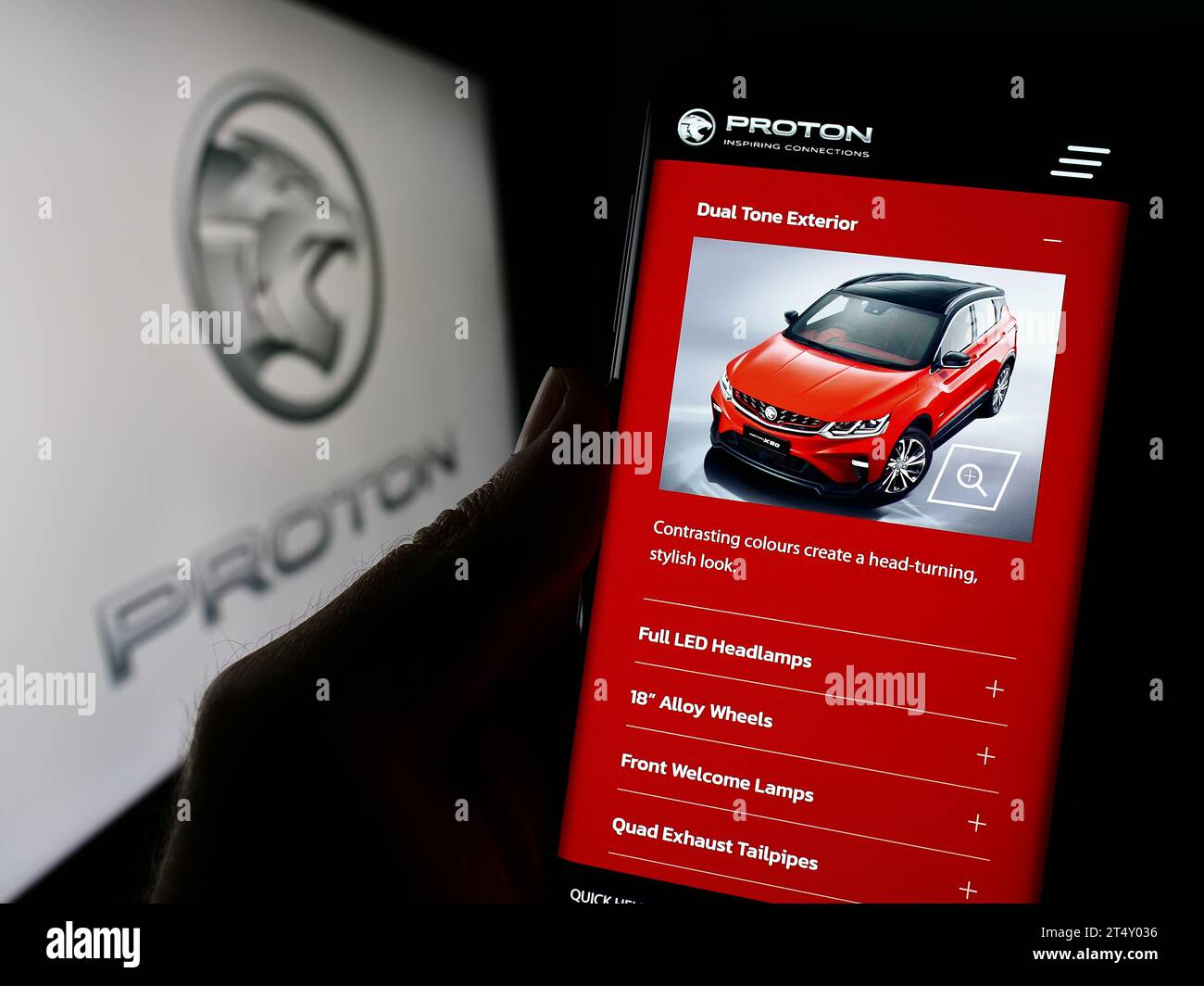 Person holding cellphone with webpage of Malaysian automotive company Proton Holdings Berhad (PHB) with logo. Focus on center of phone display. Stock Photo