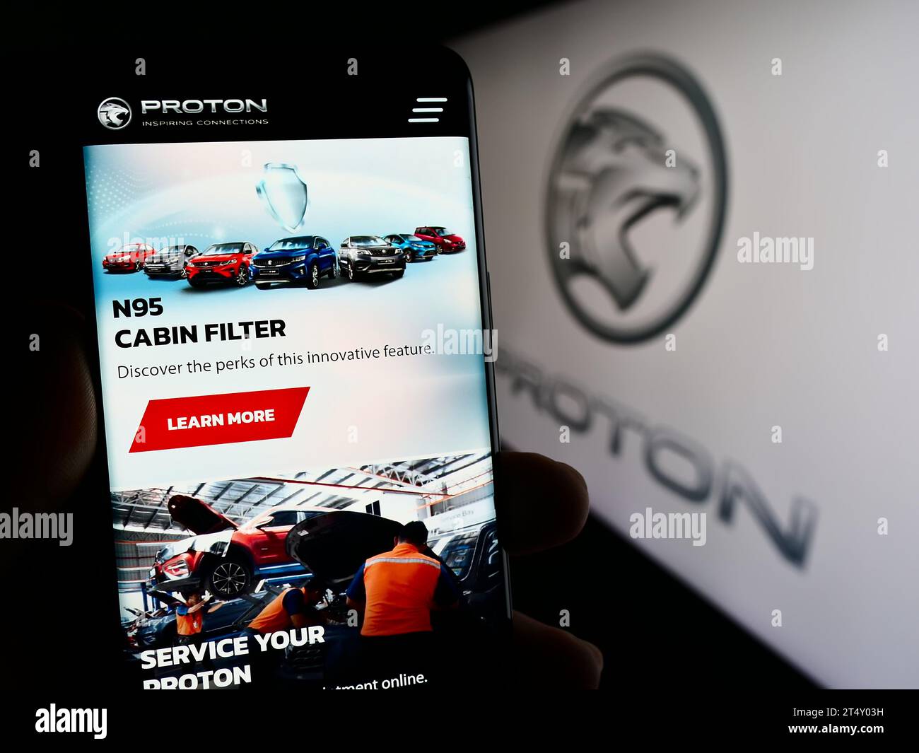 Person holding smartphone with web page of Malaysian automotive company Proton Holdings Berhad (PHB) with logo. Focus on center of phone display. Stock Photo
