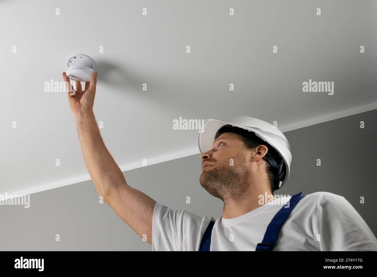 fire safety engineer installing photoelectric smoke detector on house ceiling. home security and fire alarm system Stock Photo