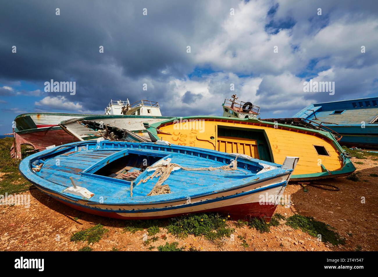 Colourful boats, refugee boats, Cimitero delle barche, boat graveyard, boat wrecks, blue cloudy dramatic sky, Lampedusa Island, Agrigento Province Stock Photo