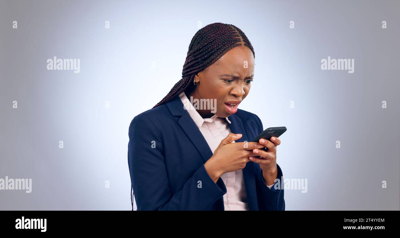 Stress, phone and confused black woman frustrated by text in studio with fake news, review or feedback on grey background. Surprise, anxiety and Stock Photo