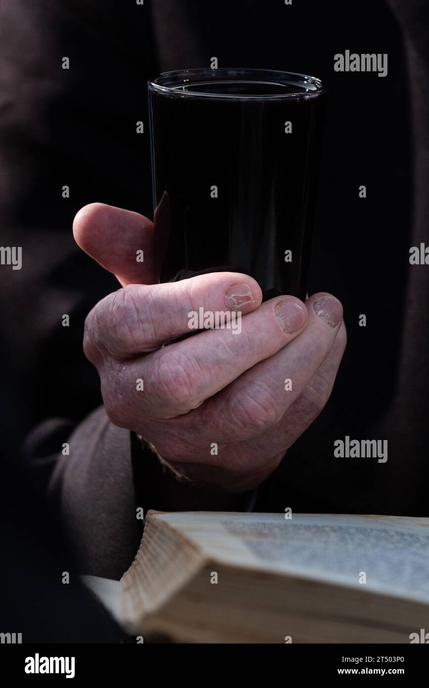 A man holds a small glass of red wine in one hand and recites a blessing for the bride and groom under the chuppah or wedding canopy at a Jewish weddi Stock Photo