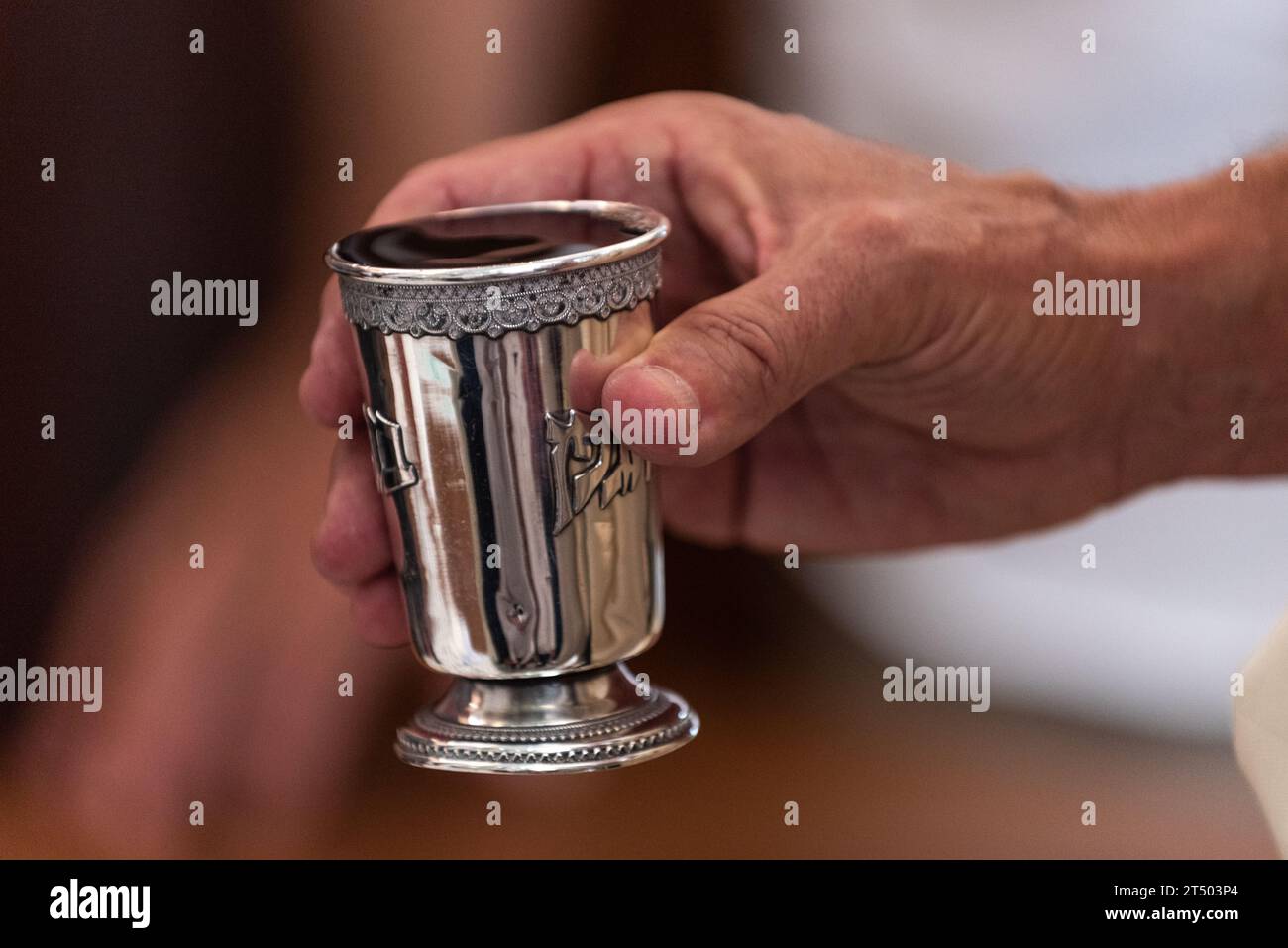 A man holds a silver cup of wine in one hand and recites a blessing for the bride and groom under the chuppah or wedding canopy at a Jewish wedding. Stock Photo