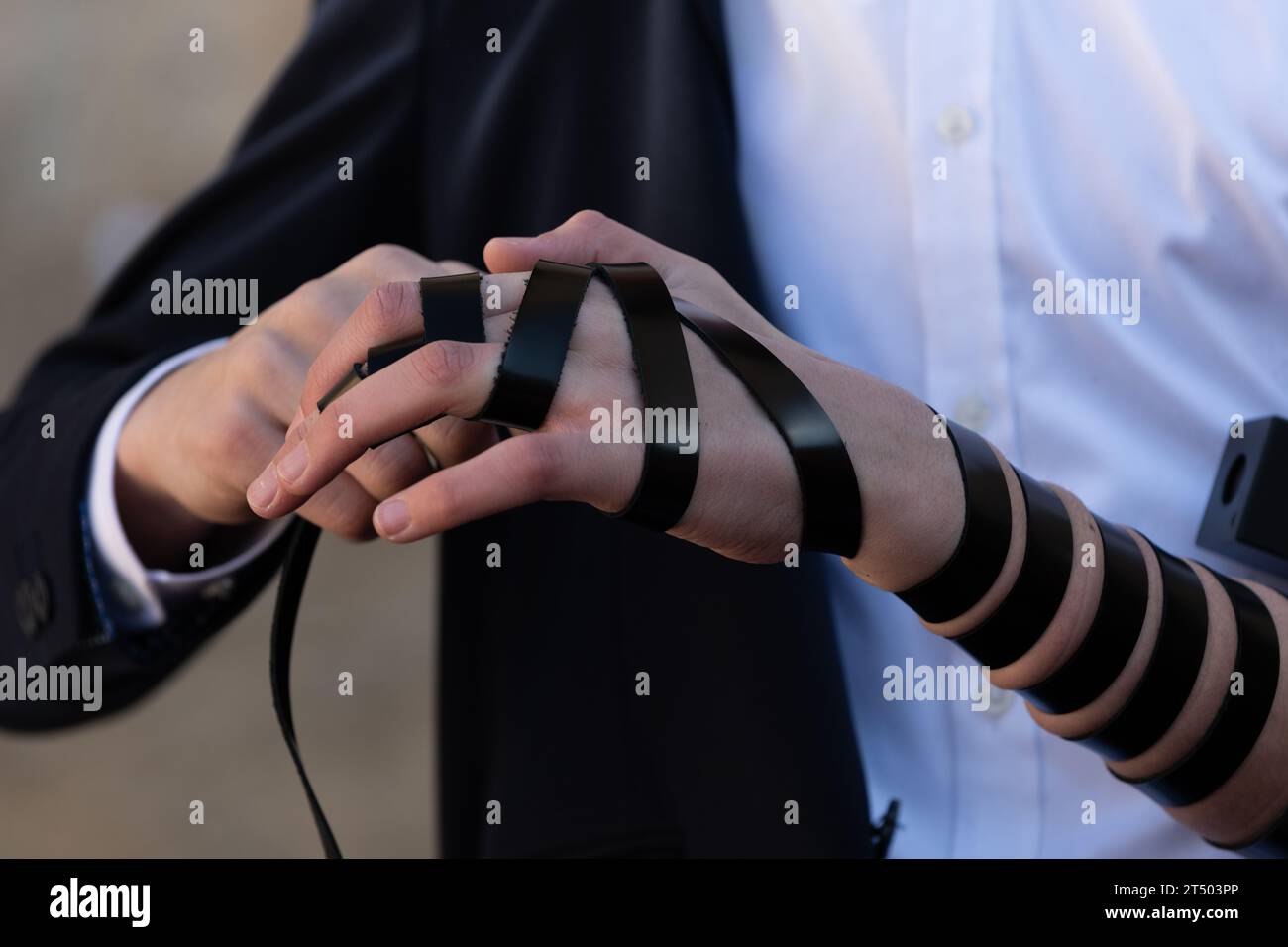A Jewish man wraps the black leather straps of his tefillin around his