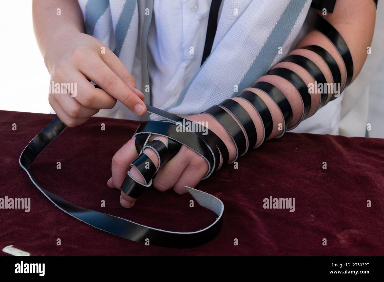 A Jewish man wraps the black leather straps of his tefillin around his