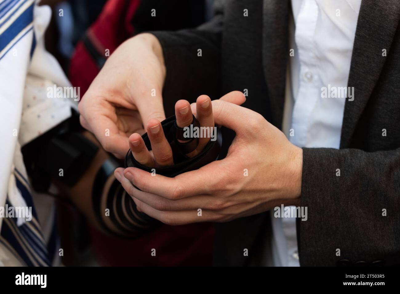 A Jewish man wraps the black leather straps of his tefillin around his