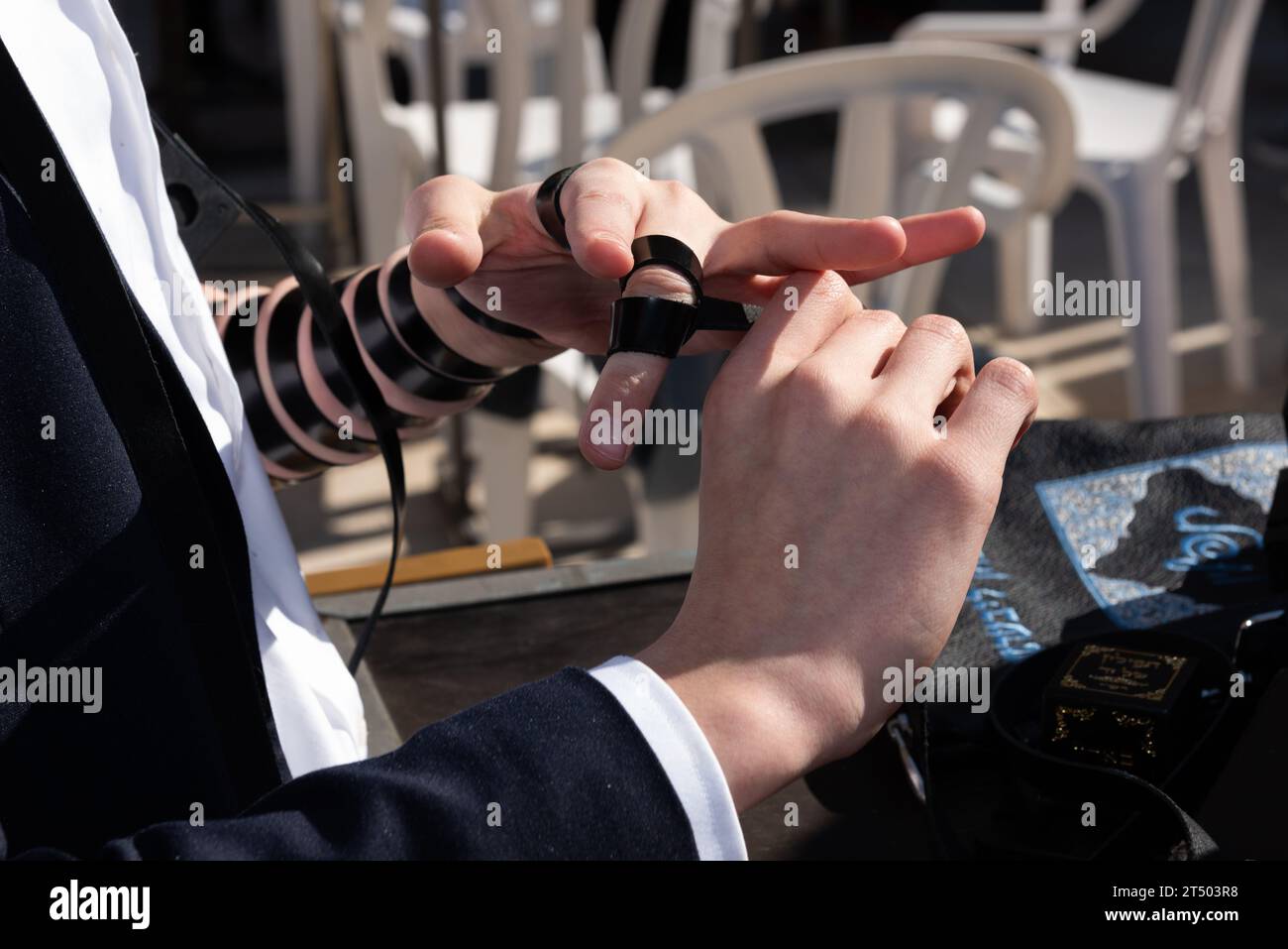 A Jewish man wraps the black leather straps of his tefillin around his