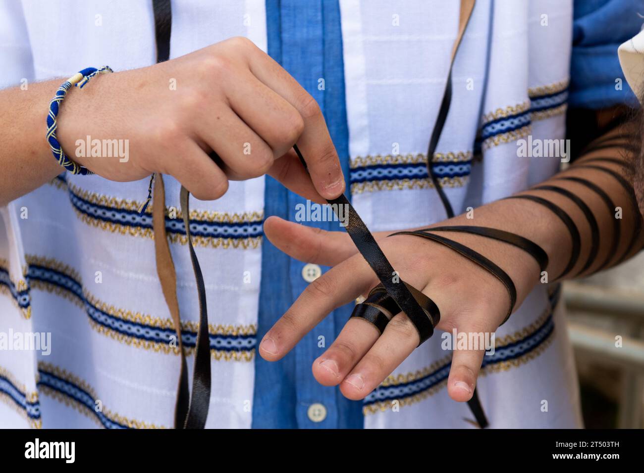 A Jewish man wraps the black leather straps of his tefillin around his