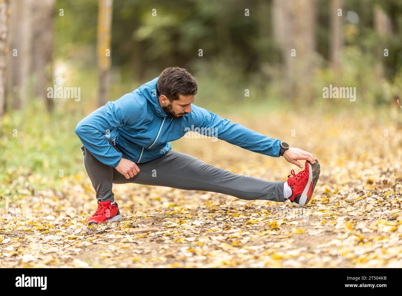 A young athlete is warming up before running training in the park. It warms the lower part of the body. Stock Photo