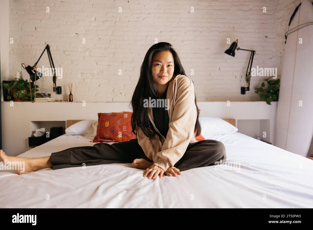Portrait of a young beautiful female sitting on bed Stock Photo - Alamy