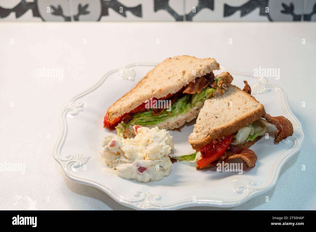 BLT, a bacon, tomato & lettuce sandwich made with oatnut bread, with a serving of potato salad on a white plate. USA. Stock Photo
