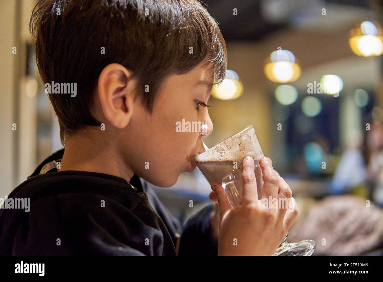 close-up portrait of latino little boy in profile in a bar drinking hot chocolate milk. Out of focus background and lighting Stock Photo