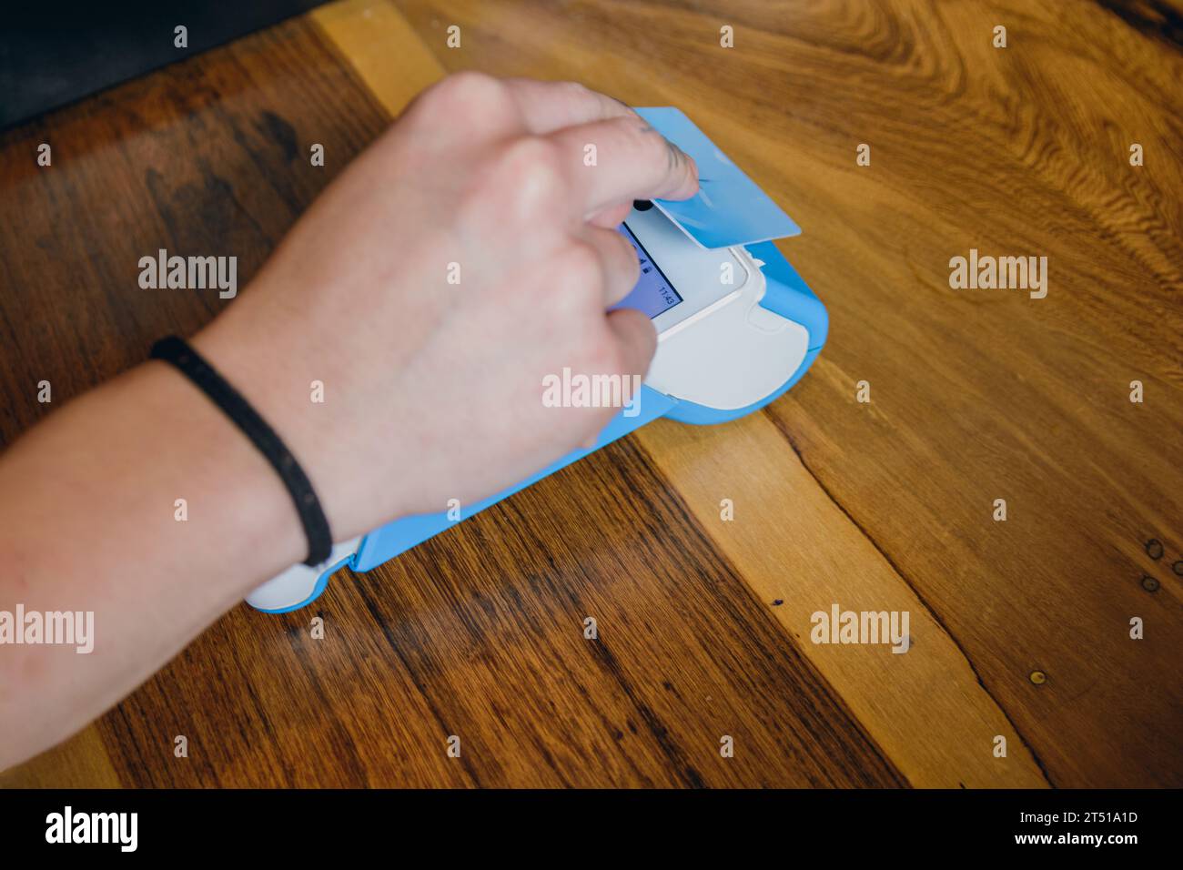 Caucasian hand of unrecognizable female waitress with debit card making payment at wireless point of sale on wooden counter of restaurant. Stock Photo