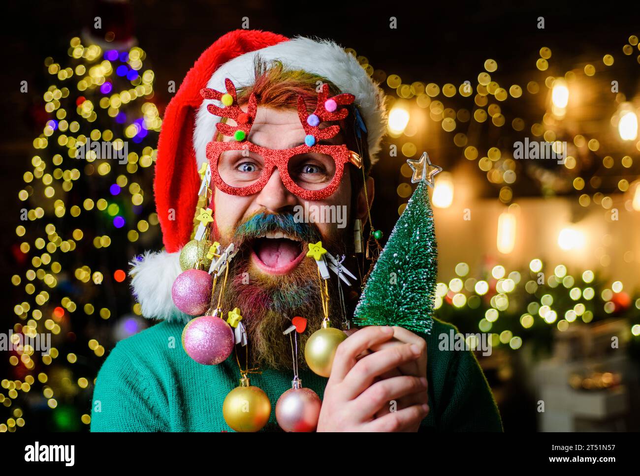 Merry Christmas and Happy New Year. Bearded man in Santa hat and party glasses with small Christmas tree. Happy Santa man with Christmas decorated bea Stock Photo
