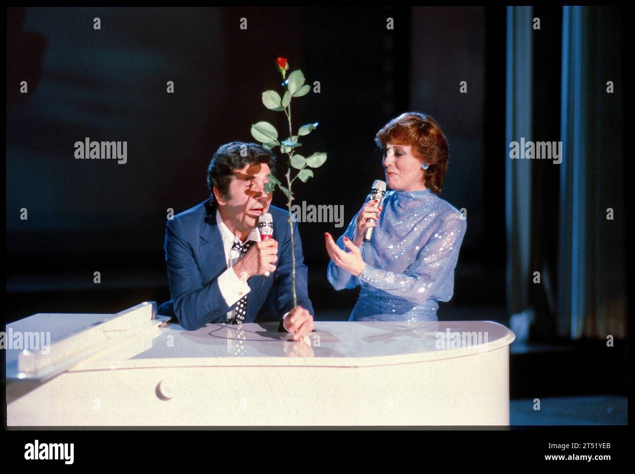 Monsieur 100.000 Volt 1982: Ich sags Dir durch die Blume Fotos: Leopold NEKULA/VIENNAREPORT e. U. âÖï ORF Caterina Valente-TV-Show Caterina xx. Mai 1982, Stadthalle, Wien . âžï https://www.palaismontcalm.ca/concert-spectacle-quebec/et-maintenant-le-spectacle-hommage-a-gilles-becaud-13-avril-2024/ . Bild: Gilbert Becaud singt mit einer roten Rose in der Hand zusammen mit Caterina Valente auf der Bühne der Wiener Stadthalle. Gilbert BÃ caud * 24. Oktober 1927 als Francois Gilbert LÃ opold Silly in Toulon, Frankreich 18. Dezember 2001 in Paris 1 war ein französischer Chansonnier. Er wurde wege Stock Photo