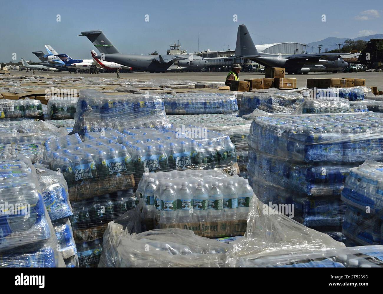1001285345W-098 PORT-AU-PRINCE, Haiti (Jan. 28, 2010) Pallets of humanitarian aid and bottled water are lined up in a staging area just off the tarmac of Aerodome de Jacmel, an airport in Port-au-Prince, while cargo planes from various nations sit at the airport's terminal facility. The multi-purpose amphibious assault ship USS Bataan (LHD 5) and the amphibious dock landing ships USS Fort McHenry (LSD 43), USS Gunston Hall (LSD 44) and USS Carter Hall (LSD 50) are participating in Operation Unified Response as the Bataan Amphibious Relief Mission by providing military support capabilities to c Stock Photo