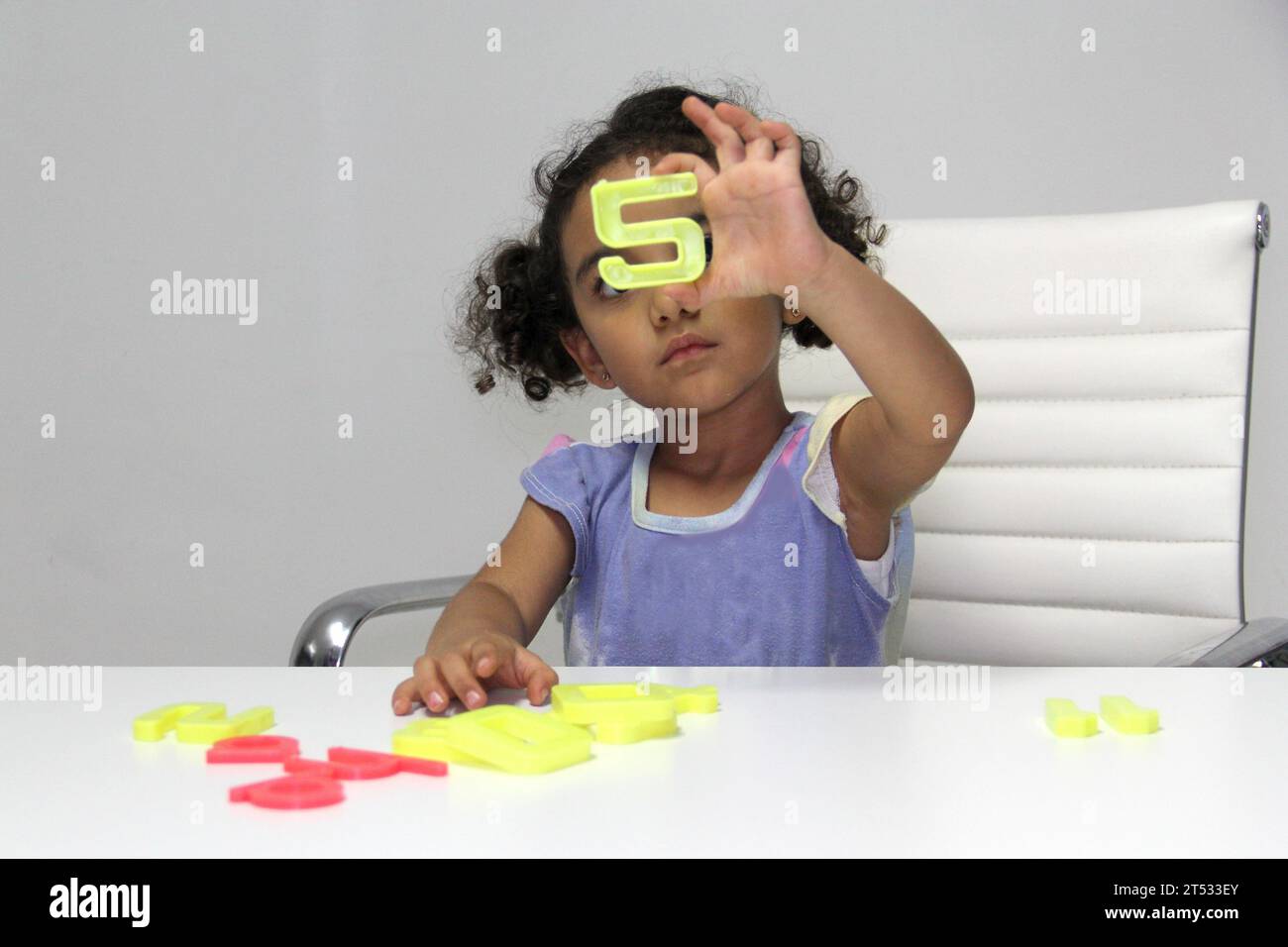 3-year-old Latina girl with brunette and curly hair plays with a game of letters and numbers for better learning within the autism spectrum Stock Photo