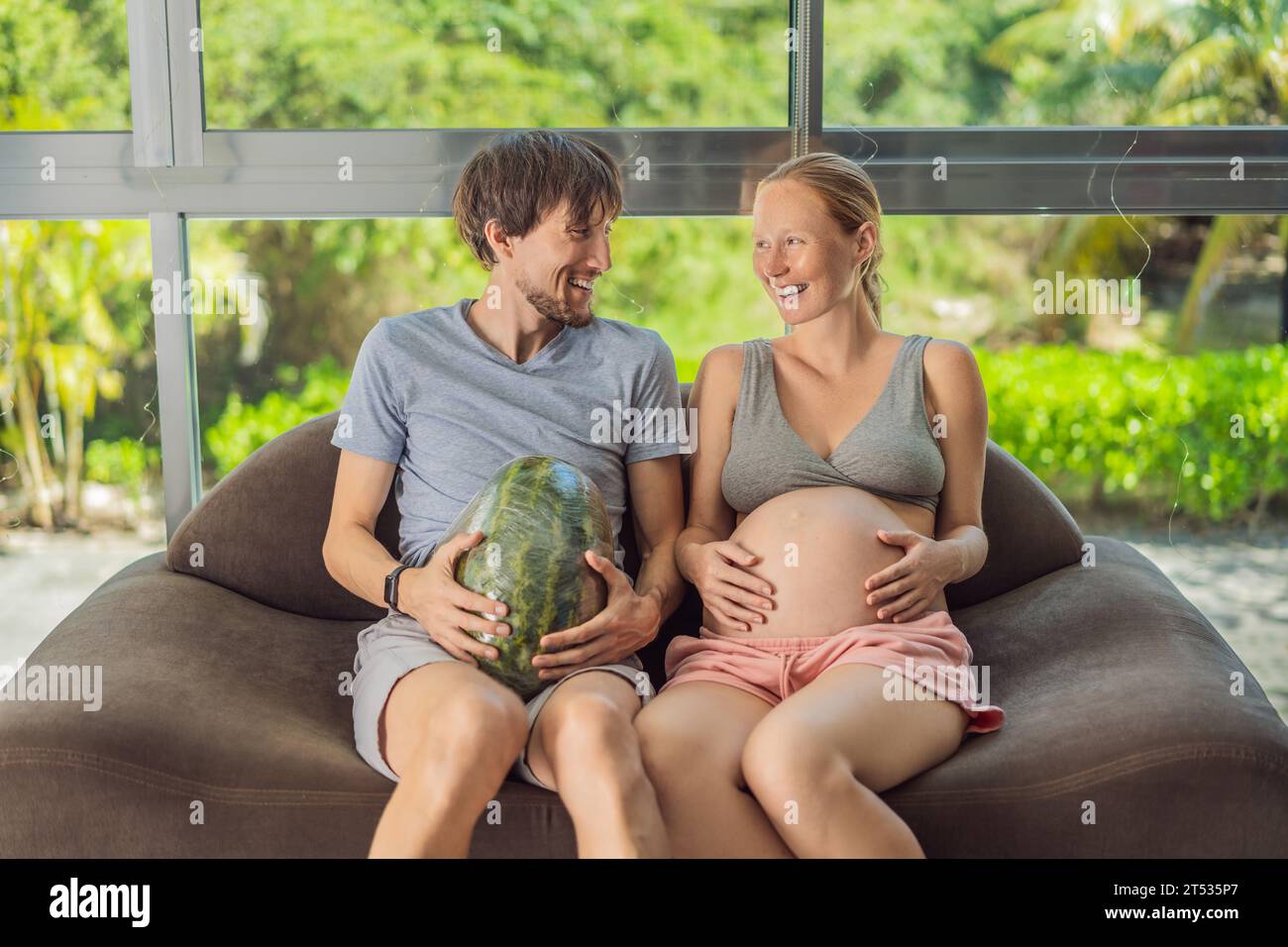 A humorous image: a pregnant woman and her husband playfully use a watermelon in place of a belly, comically highlighting the challenges of navigating Stock Photo