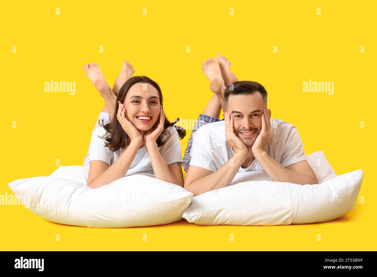 Young couple with pillows lying on yellow background Stock Photo