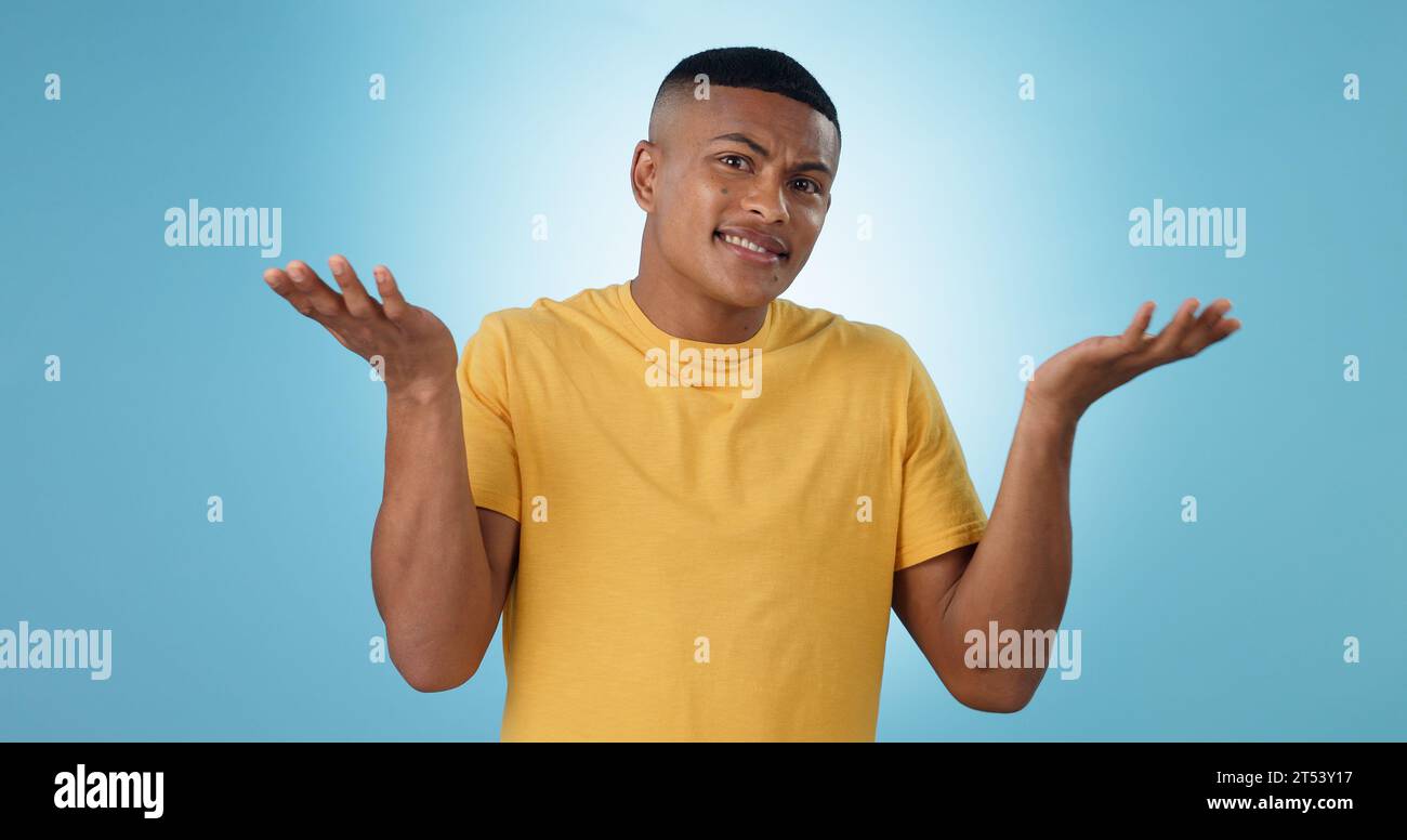 Confused, shrug and man portrait in studio with why hands on blue background space. Doubt, face and model with dont know emoji for choice, decision or Stock Photo