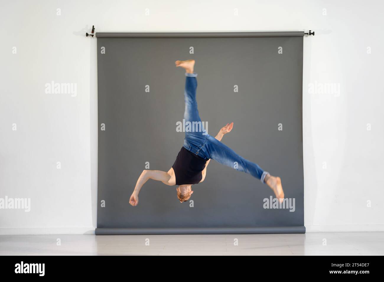 Full length of flexible talented male acrobat in casual clothes performing aerial cartwheel during rehearsal in spacious studio Stock Photo