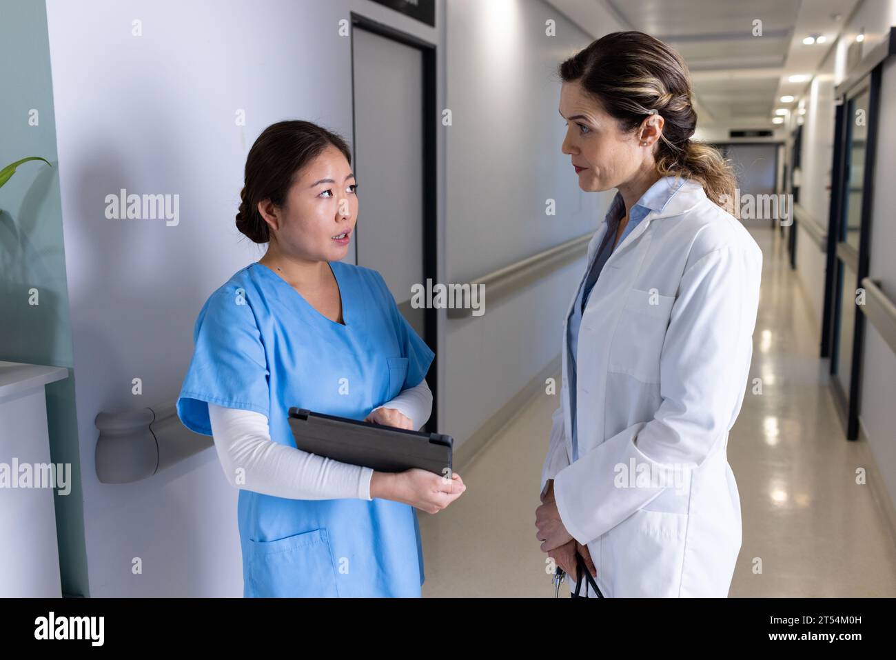 Serious diverse female doctors using tablet discussing in hospital corridor Stock Photo