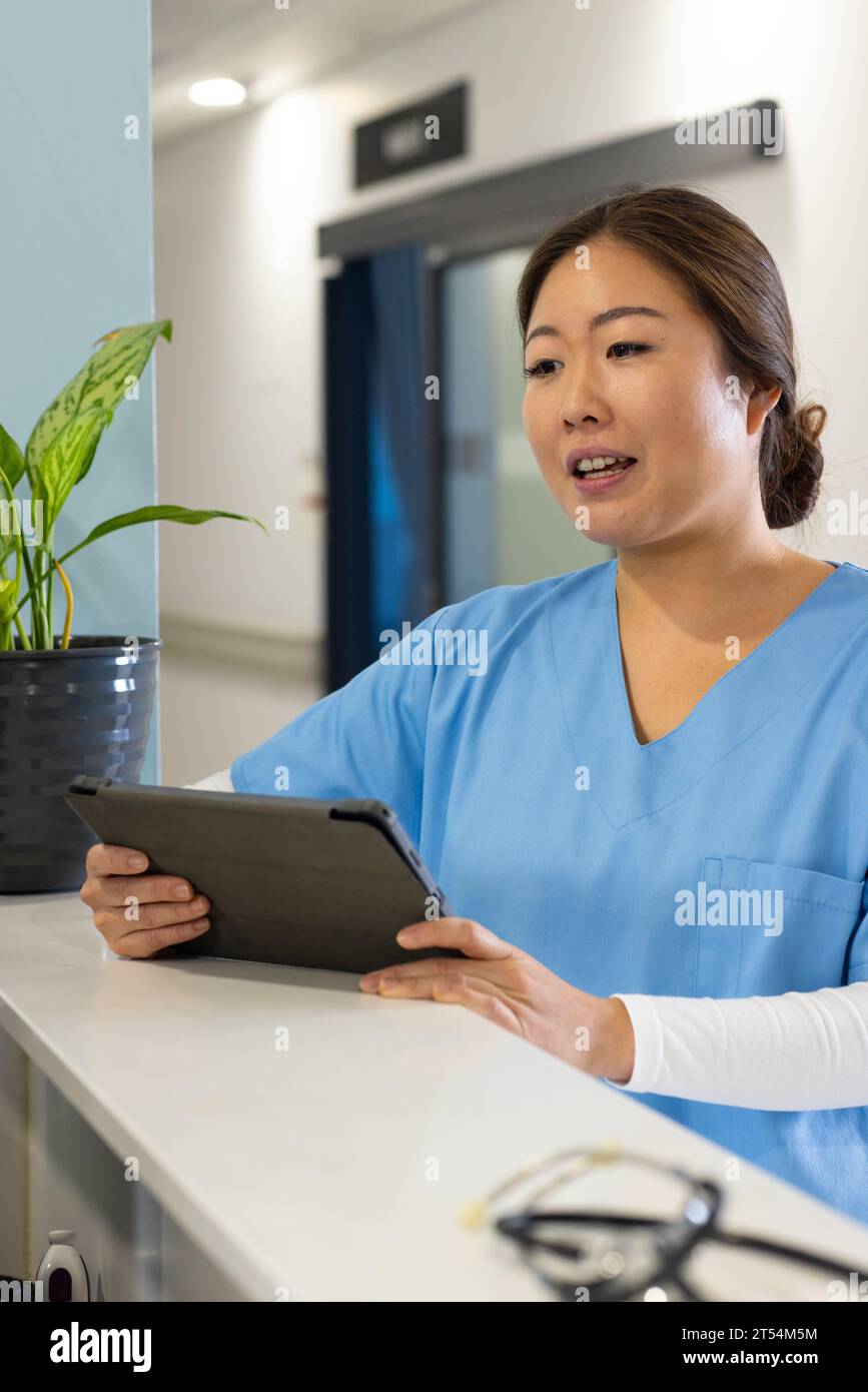 Happy asian female doctor using tablet talking at hospital reception ...