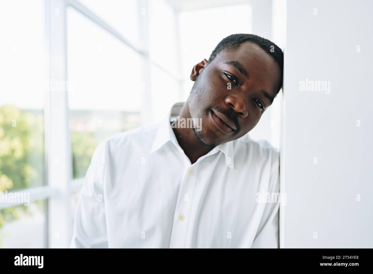 Young african man in white shirt and glasses posing near large window ...